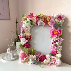 a white table topped with a pink and green flowered frame next to a plant