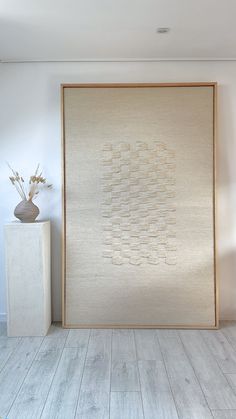 a white vase sitting on top of a wooden table next to a large wall hanging