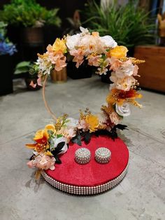 a pair of earrings sitting on top of a red box with flowers and leaves around it