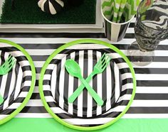 two plates with green forks and spoons on them sitting on a black and white striped table cloth