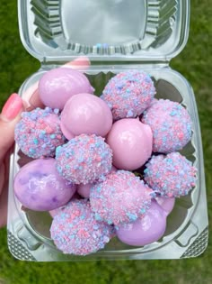 a person holding a plastic container filled with pink and blue desserts on top of green grass