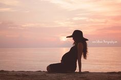 a pregnant woman sitting on the beach at sunset