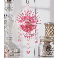 a pink beaded sun ornament hanging from a hook on a white table