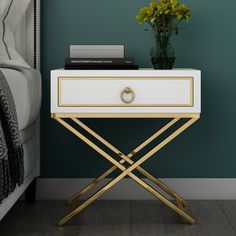 a white and gold side table with flowers on it next to a green painted wall