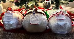 three christmas balls are wrapped in plastic and tied with red ribbon, sitting under a tree