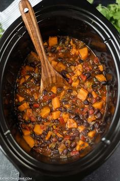 a crock pot filled with black beans and sweet potato stew next to parsley