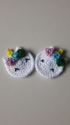 two small crocheted unicorns with flowers on their ears, one is white and the other is pink