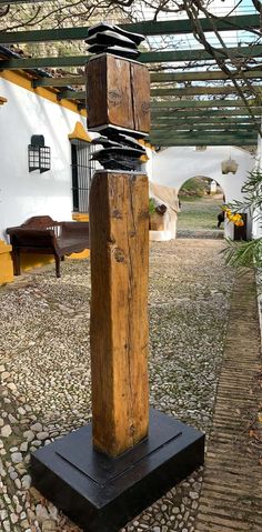 a wooden sculpture sitting on top of a stone floor next to a tree and white building