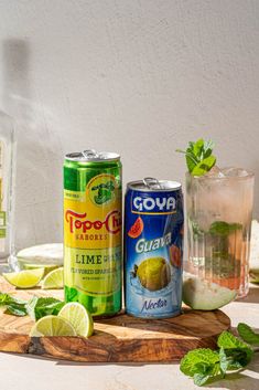 three cans of soda, limeade and mojita on a cutting board with mint leaves