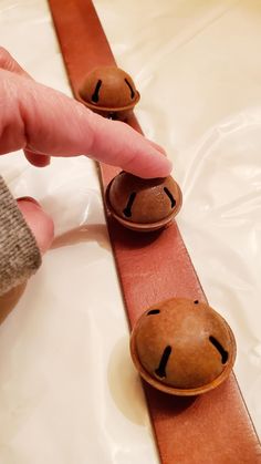 a person pointing at three wooden buttons in the shape of faces on a leather belt