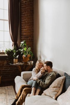 a man and woman sitting on top of a couch next to each other in front of a window