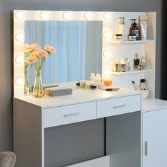 a white vanity with flowers and lights on it