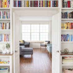 a living room filled with lots of books on top of white bookcases next to a window