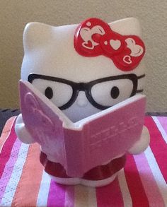 a hello kitty reading a book on top of a pink and white striped table cloth