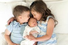 two young children cuddle together while laying on a white bed with their arms around each other