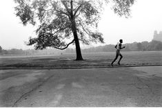 black and white photograph of a man running in a park with a tree behind him