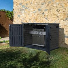 an outdoor bbq with the door open in front of a stone wall and grass