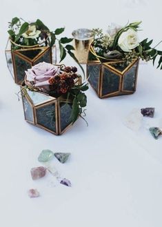 three vases filled with flowers and greenery on top of a white tablecloth