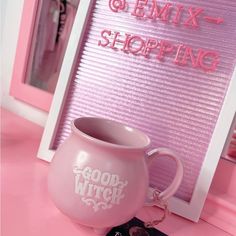 a pink mug sitting on top of a table next to a sign that says good witch