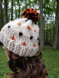 a woman wearing a white knitted hat with orange and black pom poms