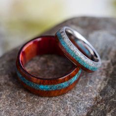 two wedding rings sitting on top of a rock with blue and brown wood inlays