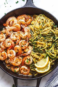 shrimp and pasta in a skillet with lemon wedges