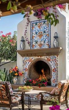 an outdoor fireplace with chairs around it and flowers on the table in front of it