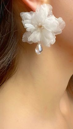 a close up of a person's ear wearing white flowers and crystal stones on them