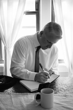 a man sitting at a table writing on a note book and holding a pen in his hand