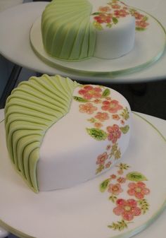 two cakes decorated with flowers and ribbons are on white plates, one has green icing