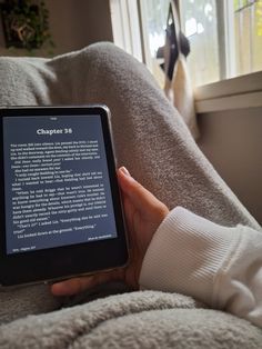 a person holding an electronic device in their hand on a couch next to a window