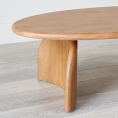 an oval wooden table with curved legs on hardwood flooring and white walls in the background