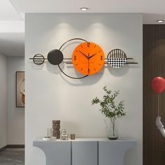 an orange clock hangs on the wall next to a vase with a plant in it