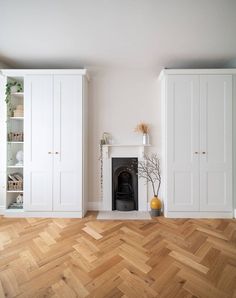 an empty room with white cupboards and a fireplace in the center, surrounded by wood flooring