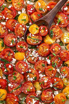 sliced tomatoes with herbs and feta cheese in a baking dish on a wooden spoon