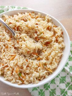 a white bowl filled with rice and carrots on top of a green napkin next to a fork