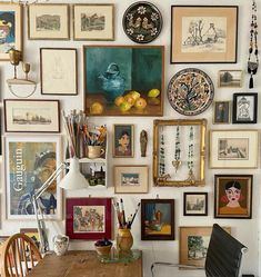 a wall full of framed pictures and art on it's side, with a wooden table in the foreground