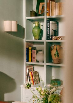 a book shelf filled with books and vases on top of each other next to a table