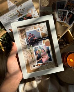 a person holding up a white frame with pictures on it and candles in the background