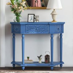 a blue painted console table with flowers and pictures on the wall in front of it