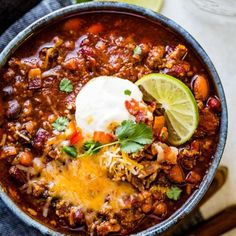 a bowl filled with chili and sour cream on top of a blue towel next to limes