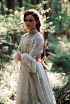 a woman in a white dress standing in the woods with her hands on her hips