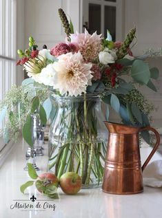 a vase filled with lots of flowers sitting on top of a counter next to an apple