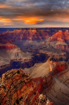 the sun is setting at the edge of the grand canyon, with clouds in the sky