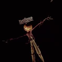 a scarecrow holding a sign that says halloween town on it's head in the dark