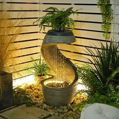 an outdoor fountain with plants and rocks in the center is lit up by water flowing from it's sides