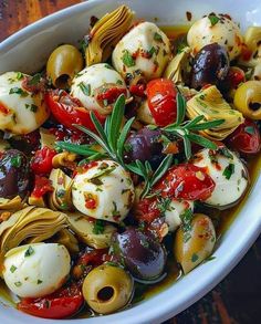 a white bowl filled with olives, tomatoes and other vegetables on top of a wooden table