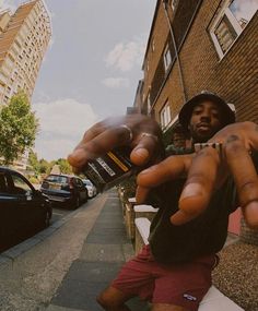 a man pointing at the camera while standing on a sidewalk with his hand in front of him