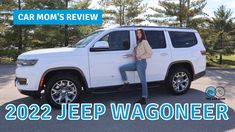 a woman sitting on the hood of a white jeep parked in a parking lot next to trees