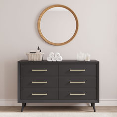 a black dresser with gold handles in front of a white wall and a round mirror above it